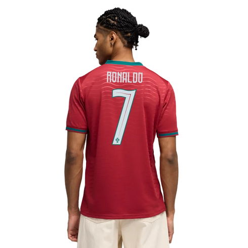 Back of a man wearing a red Portugal soccer jersey with "RONALDO 7" printed on the back. He has braided hair and wears light-colored shorts against a black background.
