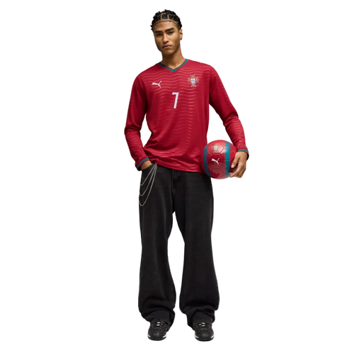 A man in a red long-sleeve Portugal soccer jersey (number 7) and baggy black jeans with a chain, holding a red soccer ball against a black background.