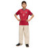 A boy posing in a red soccer jersey with the number 7, wide-leg cream trousers, and black sneakers against a black background.