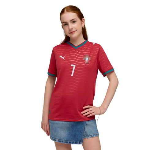 A young woman with red hair wears a red Portugal soccer jersey with number 7 and a denim skirt, posing against a black background.