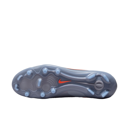 Bottom of a grey Nike soccer cleat with light blue studs and an orange swoosh on a black background. Translucent soleplate features circular traction patterns.