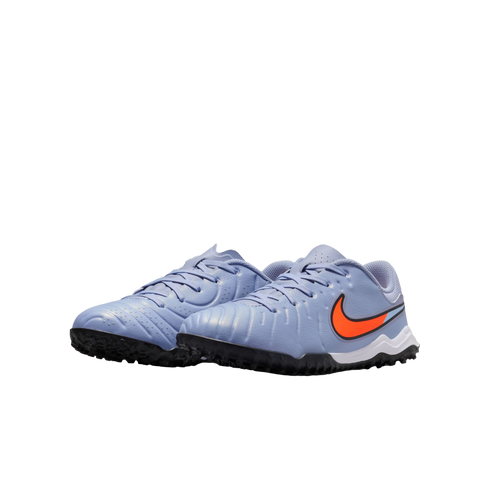 A pair of light blue Nike turf soccer shoes featuring a bright orange swoosh and black rubber soles, set against a black background.
