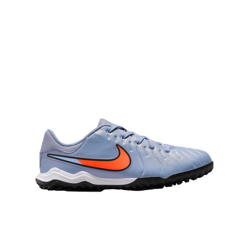 A light blue Nike soccer turf shoe with a large orange swoosh, white midsole, and black knobby outsole, set against a plain black background.