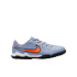 A light blue Nike soccer turf shoe with a large orange swoosh, white midsole, and black knobby outsole, set against a plain black background.