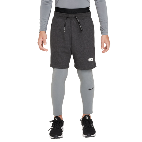 A person wearing grey Nike athletic wear, including fleece shorts over compression leggings and black sneakers, against a solid black background.