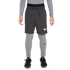 A person wearing grey Nike athletic wear, including fleece shorts over compression leggings and black sneakers, against a solid black background.