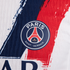 Close-up of the Paris Saint-Germain football club crest on a white jersey with textured red and blue brushstroke stripes.