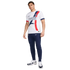 A male model wearing a white Paris Saint-Germain jersey with blue and red graphic details, navy Nike joggers, and white sneakers against a white background.