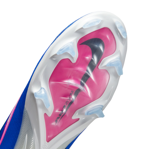 Underside of a blue and white Nike soccer cleat with a pink soleplate, a large black Nike swoosh, and clear triangular studs against a black background.