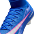 A close-up of a blue Nike soccer cleat with pink and white accents, blue laces, and a textured upper against a black background.