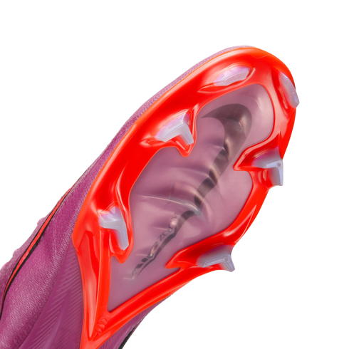 Close-up of a purple Nike soccer cleat's red and translucent sole, featuring white studs and a visible Air Zoom unit through a clear panel.
