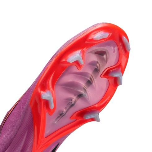 Close-up of the soleplate of a pink and orange Nike soccer cleat, showing white studs and an "Air Zoom" unit visible through the translucent pink center.