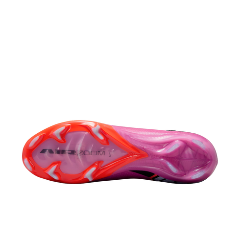 Underside view of a pink and orange Nike soccer cleat with "AIR ZOOM" branding and translucent studs, set against a solid black background.
