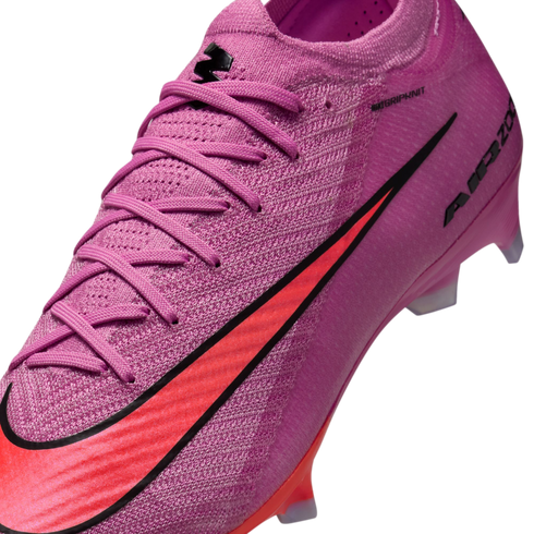 Close-up of a pink Nike soccer cleat featuring a textured Gripknit upper, matching laces, and a bold red swoosh with black outline against a dark background.