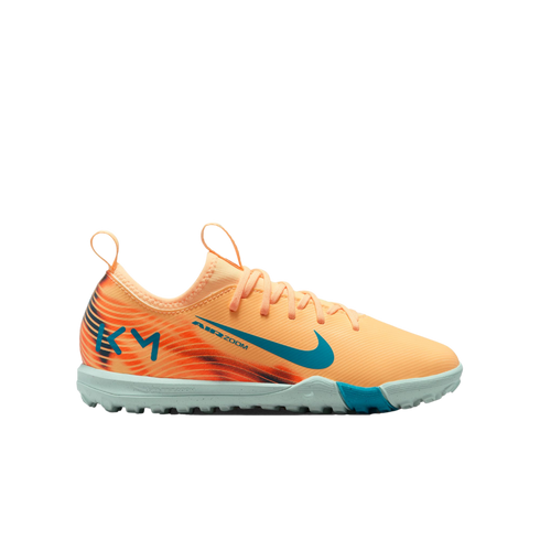 Profile view of a peach Nike turf soccer shoe with teal accents, a light blue sole, and "KM" branding on the heel against a black background.
