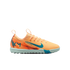 Profile view of a peach Nike turf soccer shoe with teal accents, a light blue sole, and "KM" branding on the heel against a black background.