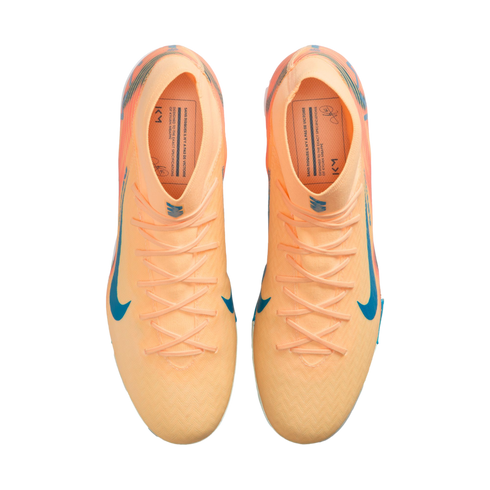 Top-down view of peach-colored Nike soccer cleats with blue swooshes and Kylian Mbappé branding on the insoles, against a black background.