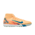 Side profile of a pale orange Nike Mercurial turf soccer shoe with teal accents and Kylian Mbappé's "KM" logo on the heel, set against a black background.