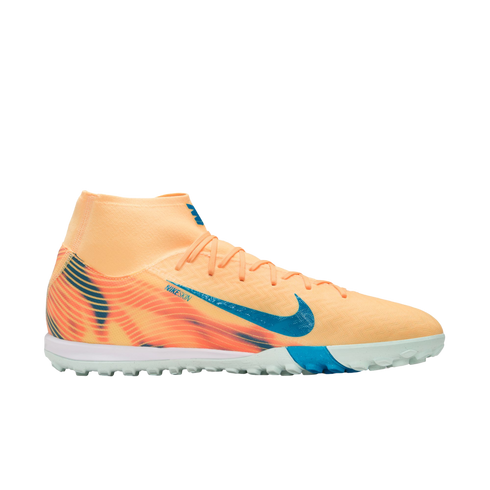 A peach-colored Nike turf soccer shoe with blue accents and a high-top collar, shown in profile against a black background.