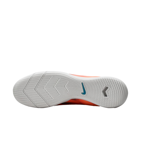 White textured rubber sole of an orange Nike indoor soccer shoe with a blue swoosh logo, shown against a black background.