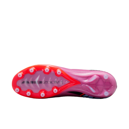 The soleplate of a pink Nike Air Zoom soccer cleat with red accents and white circular studs against a black background.