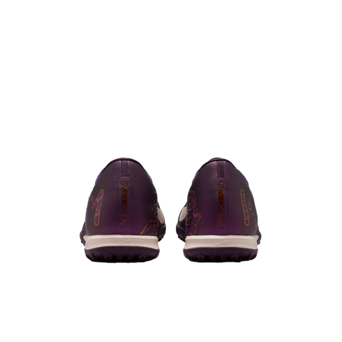 Rear view of a pair of dark purple soccer turf shoes with "MERCURIAL" printed on the heels, featuring cream midsoles and set against a plain white background.