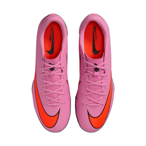A top-down view of a pair of pink Nike Mercurial soccer cleats with bright orange Nike swooshes and orange interiors, centered on a solid black background.