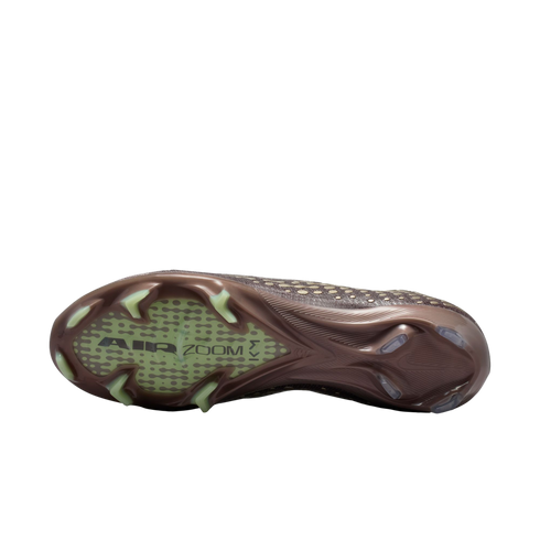 Sole of a bronze Nike soccer cleat with lime green studs and "AIR ZOOM KM" branding on a translucent forefoot plate, against a black background.