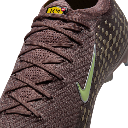 Close-up of a mauve Nike soccer cleat with a knit texture, lime green swoosh, and yellow KM logo on the tongue. Gold dot patterns are visible on the side.