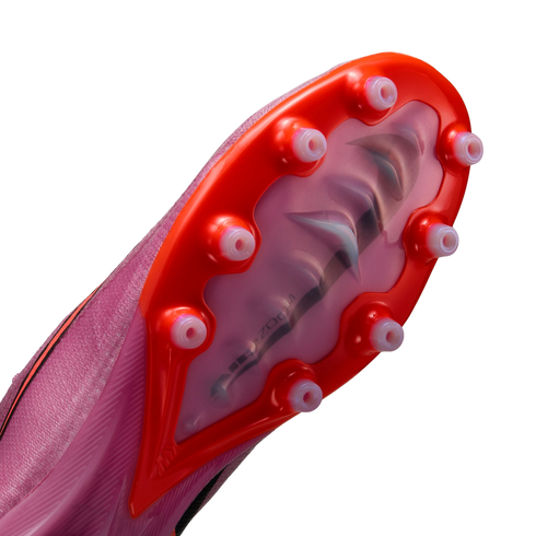Close-up of a pink Nike soccer cleat's soleplate with bright orange accents and translucent conical studs, showing a visible Air Zoom unit inside.