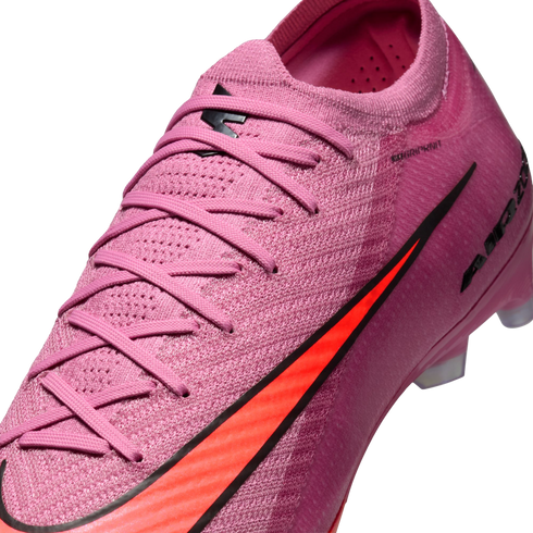 Close-up of a pink Nike soccer cleat featuring a textured knit upper, matching pink laces, and a vibrant orange swoosh logo with black trim.