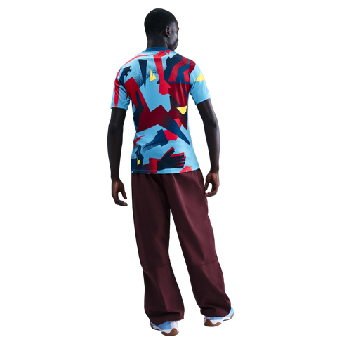 Back view of a person wearing a colorful geometric print T-shirt, loose maroon trousers, and light blue sneakers, standing against a black background.