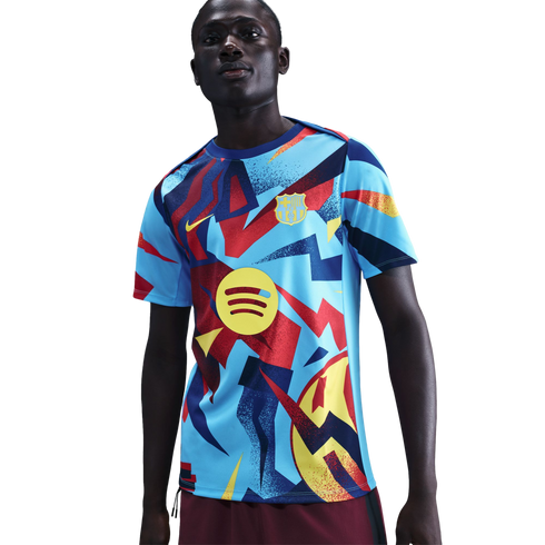 A man wearing an FC Barcelona pre-match jersey with a light blue base and bold, abstract patterns in red, yellow, and dark blue. Features include the Nike swoosh and Spotify logo.
