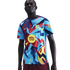 A man wearing an FC Barcelona pre-match jersey with a light blue base and bold, abstract patterns in red, yellow, and dark blue. Features include the Nike swoosh and Spotify logo.