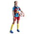 A young girl wearing a patterned soccer jersey, red shorts, and yellow socks stands against a black background, holding a soccer ball under her arm.