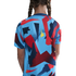 Back view of a person with braided hair wearing a light blue T-shirt with a bold geometric pattern in red, blue, and yellow.