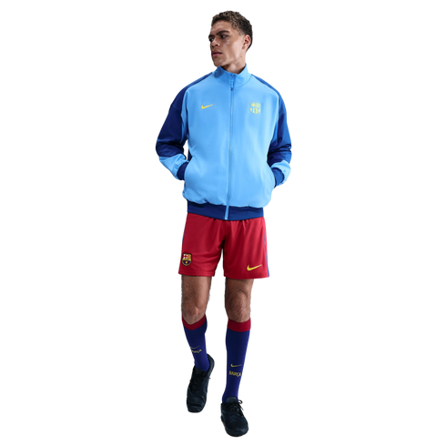 Man modeling a light blue and navy FC Barcelona track jacket, red shorts, and tall blue socks against a solid black background.