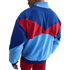 Rear view of a royal blue, light blue, and red color-blocked track jacket with geometric panels, worn with matching red shorts against a black background.