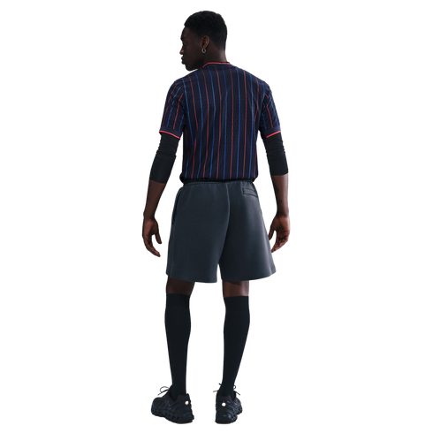 A full-body rear view of a model wearing a dark pinstriped jersey, black athletic arm sleeves, charcoal gray athletic shorts, black knee-high socks, and black sneakers against a white background.
