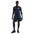 A man models a navy blue USA soccer jersey with red and blue pinstripes, charcoal gray shorts, black knee-high socks, and black sneakers.