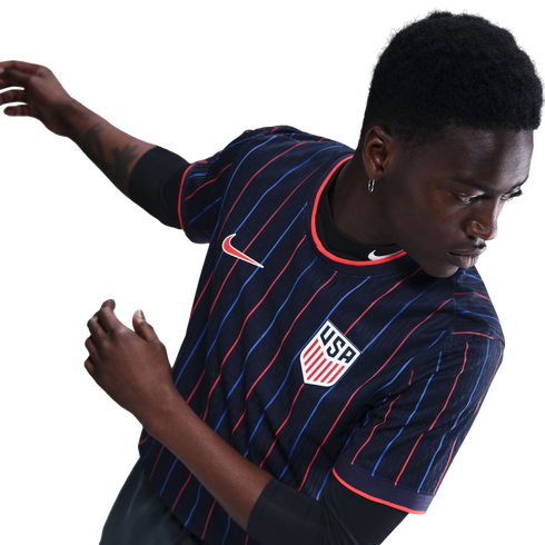A Black man in a navy USA soccer jersey with red and blue pinstripes, featuring the Nike logo and team crest. He is in a dynamic pose against a white background.