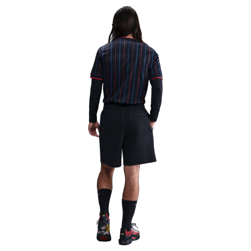 A back view of a person wearing a navy and red pinstriped jersey, black shorts, and black and red sneakers against a white background.