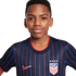 A young Black boy wearing a navy blue USA soccer jersey with red and blue stripes, a Nike swoosh, and the USA crest, posed against a white background.