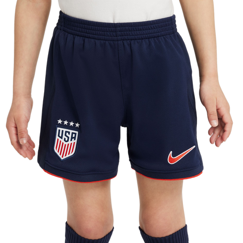 A child wears navy blue Nike soccer shorts featuring the USA national team crest, four stars, and red trim against a white background.
