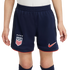 A child wears navy blue Nike soccer shorts featuring the USA national team crest, four stars, and red trim against a white background.