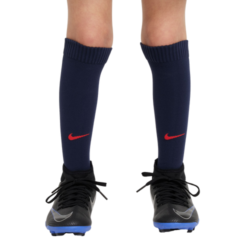 A close-up of a person's legs wearing navy blue Nike soccer socks with red swooshes and black cleats with blue soles against a white background.
