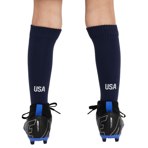 Rear view of a person's lower legs wearing navy blue USA soccer socks and black Nike Mercurial cleats with bright blue accents against a white background.