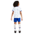 Back view of a child wearing a white USA soccer kit with geometric patterns, blue shorts, white socks with "USA" text, and black cleats.