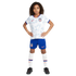 A young child in a white USA soccer uniform, blue shorts, and black cleats stands with hands on hips against a white background.