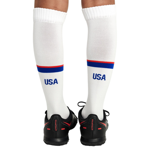 Rear view of a person's legs wearing white knee-high USA socks with red and blue stripes and black Nike Phantom soccer shoes.